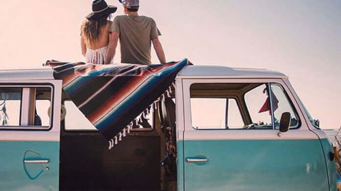 a cute couple enjoying the view of the ocean, sitting on a blanket atop a blue vintage VW van