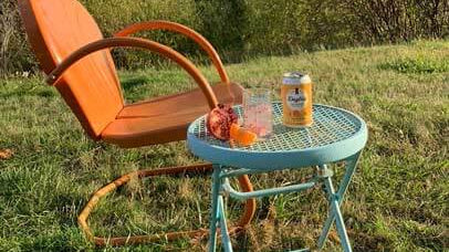 daytrip cbd infused sparkling water sitting on a side table next to an outdoor lounge chair on grass