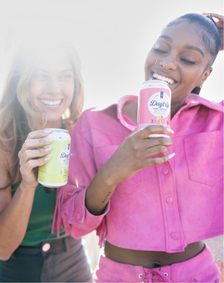 Two women smiling and each enjoying a can of Daytrip sparkling water