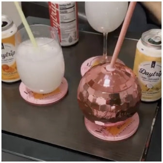 A cocktail glass scene showing cans of Daytrip sparkling water and a disco ball cocktail glass next to a highball glass filled with cocktails.