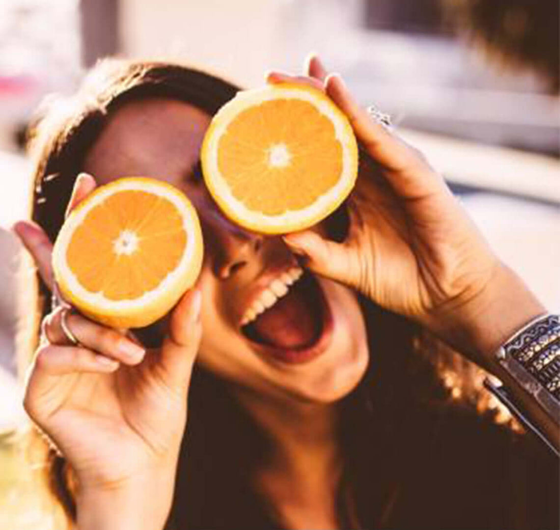 Young woman holding two orange slices over her eyes laughing as she looks up