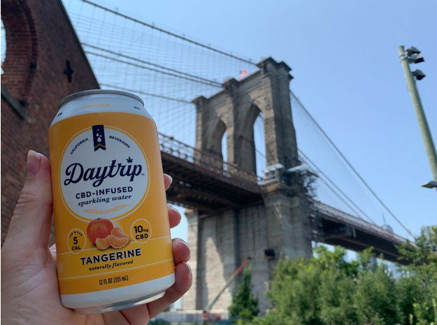 A can of daytrip cbd sparkling water held up by hand in front of the brooklyn bridge