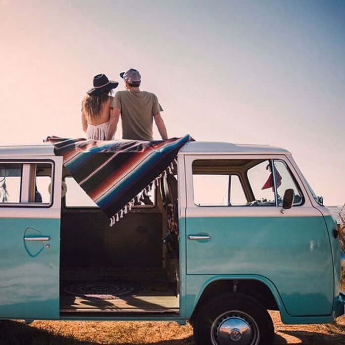 a cute couple enjoying the view of the ocean, sitting on a blanket atop a blue vintage VW van