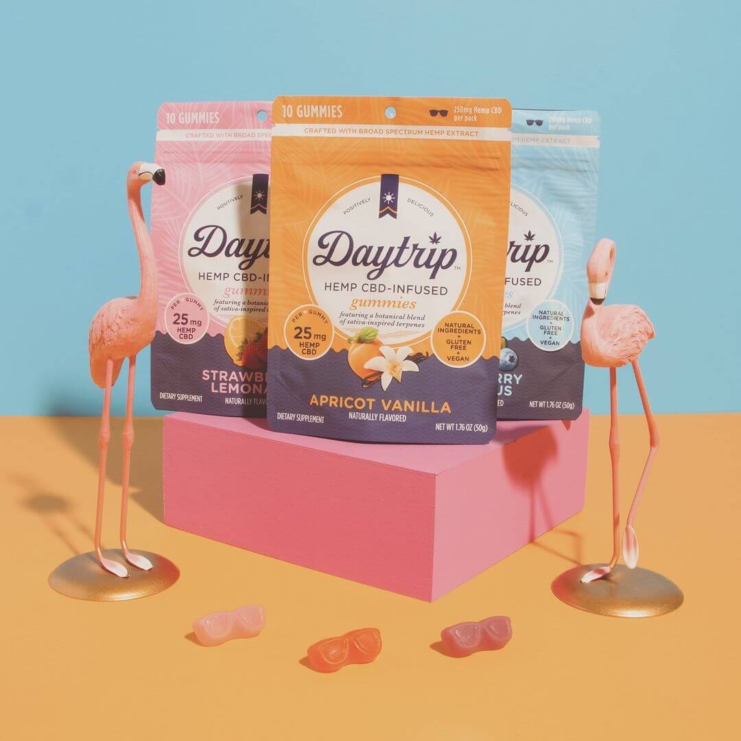 Playful colorful collection of Daytrip CBD infused gummies and toy flamingos on an orange and blue background