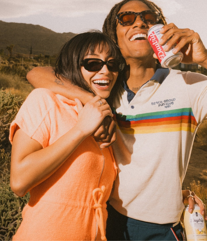 Two models holding hands with their arms around each other. One of them holding a can of Daytrip sparkling water.