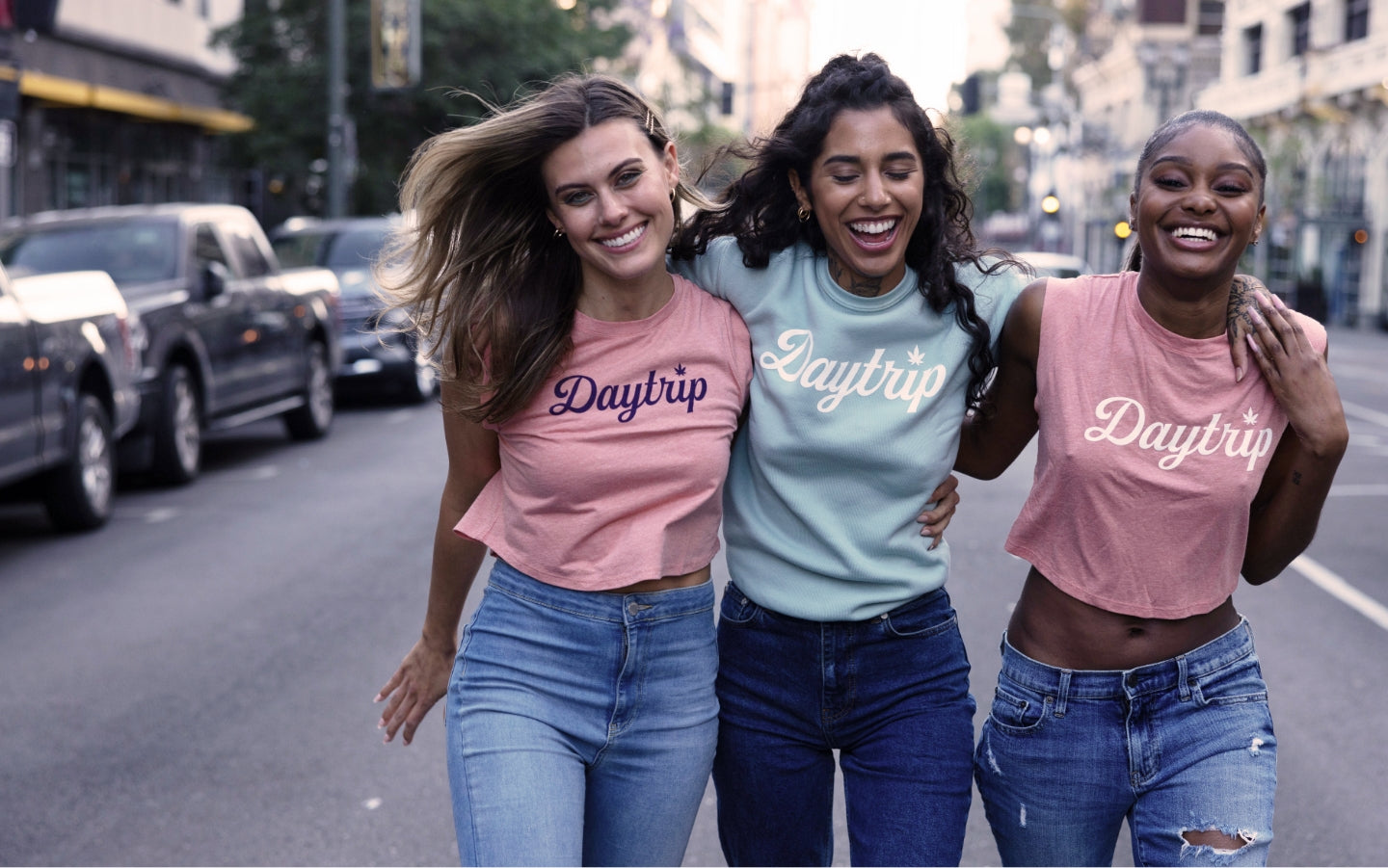 Three women smiling as they walk down a busy street in downtown los angeles in Daytrip shirts