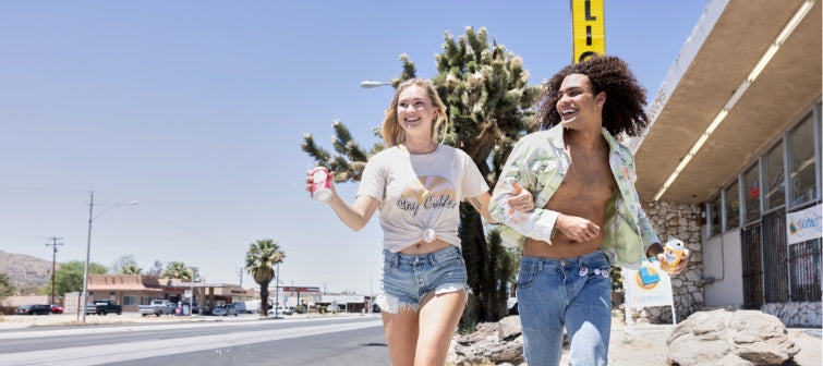 Young man and young woman running down the sidewalk in front of a cactus smiling and holding cans of Daytrip sparkling water.