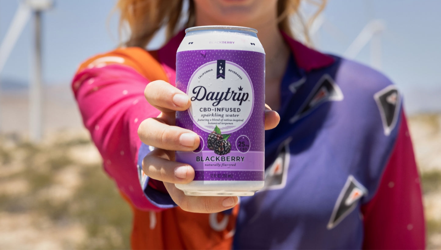 A woman holding up a can of Daytrip blackberry sparkling water. 